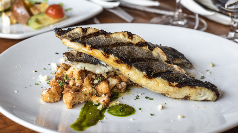 grilled branzino on a plate with a green sauce