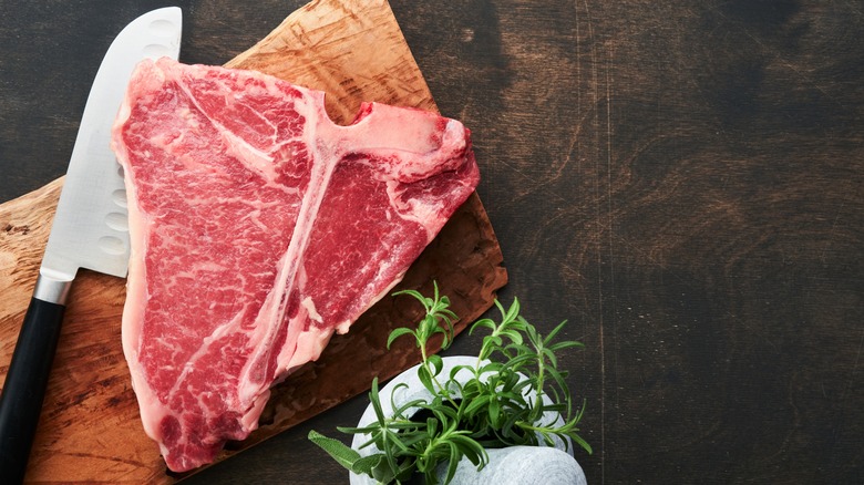 a porthouse steak on a cutting board next to fresh rosemary
