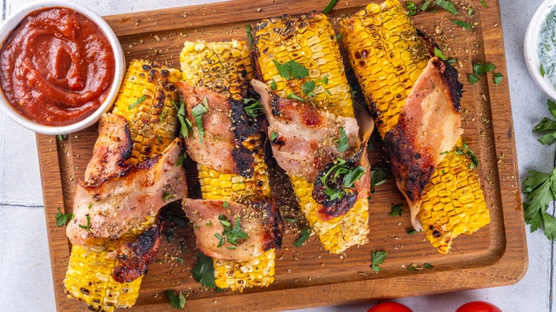 Bacon wrapped corn on the cob on a wooden cutting board