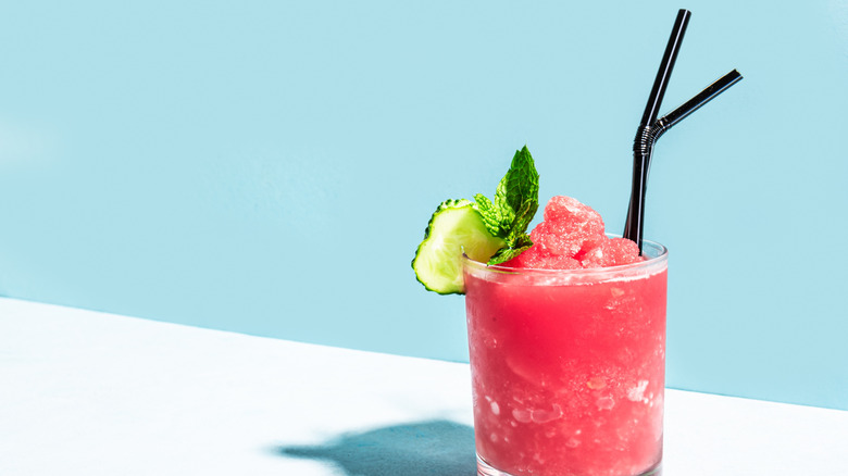 A glass of partially frozen watermelon juice garnished with a cucumber and a sprig of mint.