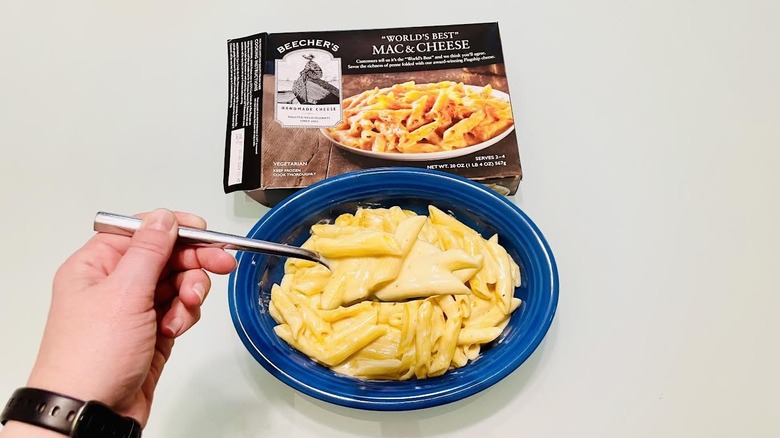 A hand gets a forkful of Beecher's mac & cheese from a blue bowl, with the empty frozen food box sitting adjacent