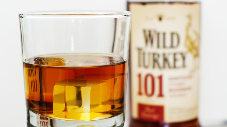 A glass of whiskey with ice, with a Wild Turkey 101 bottle behind it
