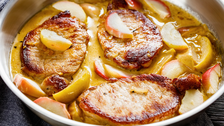 pork chops in a skillet with apple juice and sliced apples