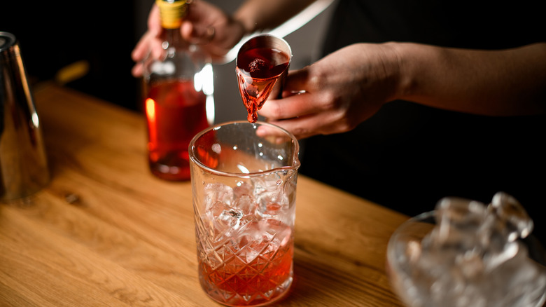 Someone pours spirits from a jigger into a cocktail pitcher